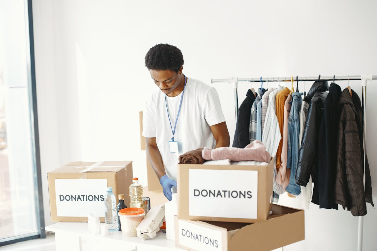 A volunteer organizes donations in a community center, featuring boxes labeled Donations and a clothing rack.